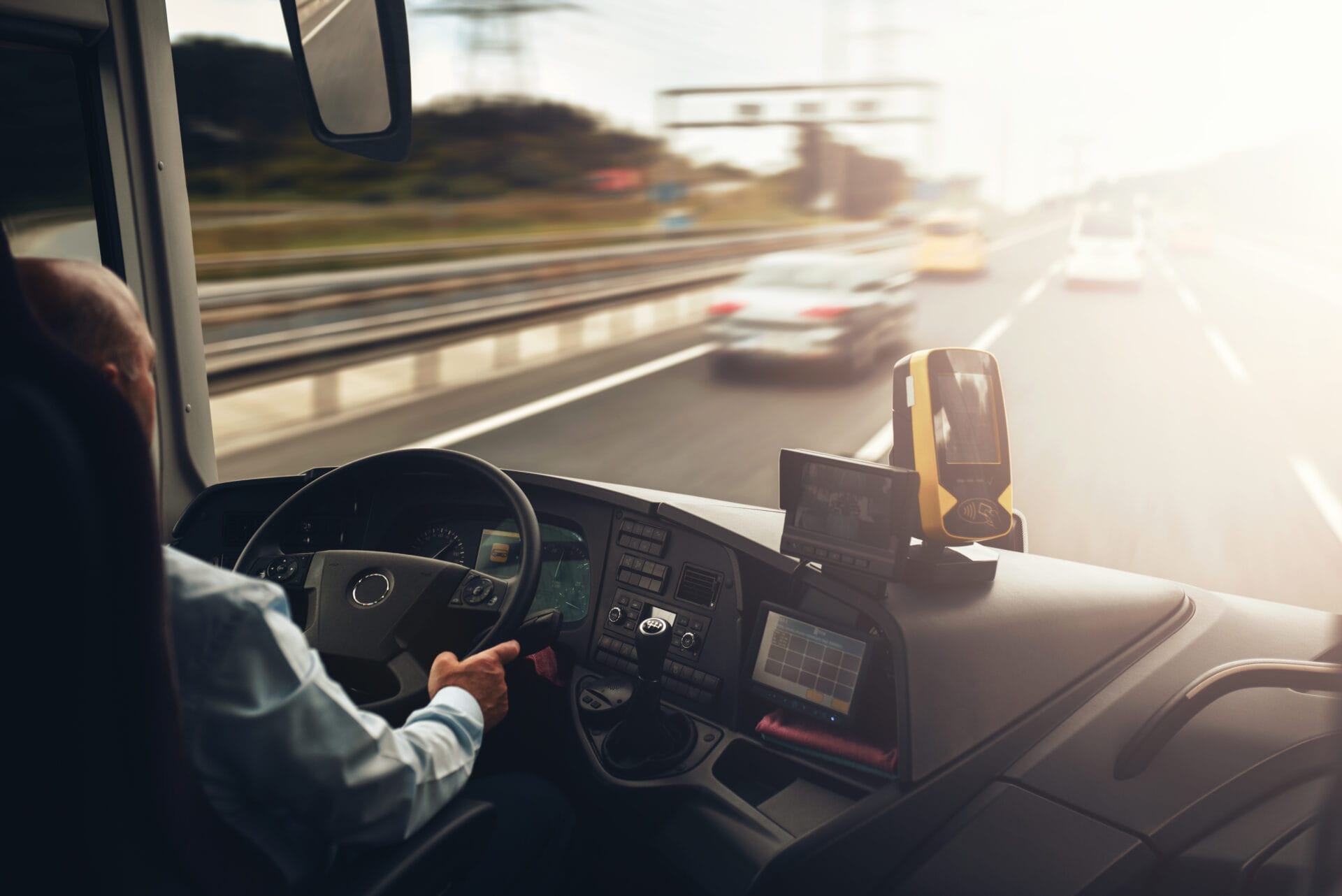 Image of a bus driver from behind, driving down a highway at sunset